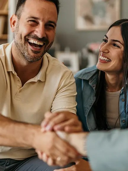 A man and woman smiling and shaking hands in a warm indoor setting.